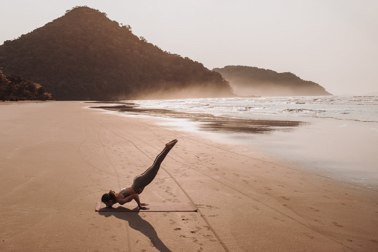 A woman practicing yoga on a serene sandy beach with scenic views during sunset.